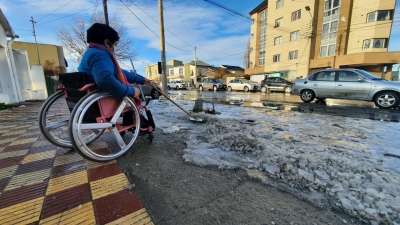 En silla de ruedas, limpia la vereda para que ningún peatón sufra un accidente